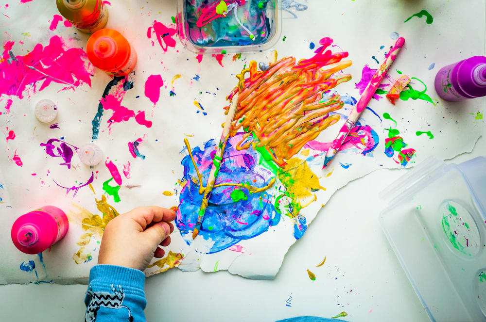 A colourful painting and paint-covered hands, illustrating creative exploration